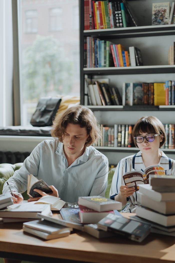 Two young adults reading and studying in a cozy library setting with bookshelves.