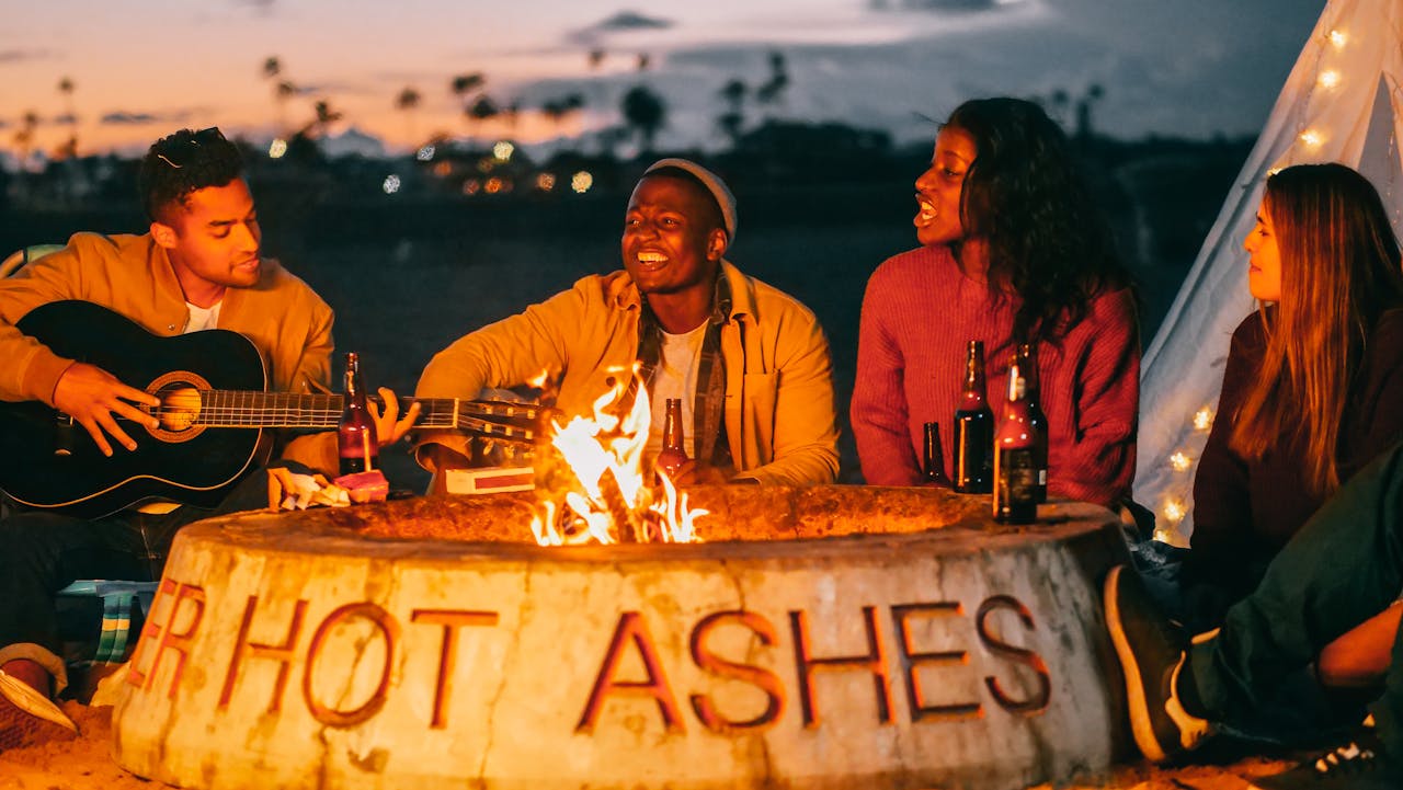 our-story Group of friends having a fun beach bonfire with music and drinks at night.